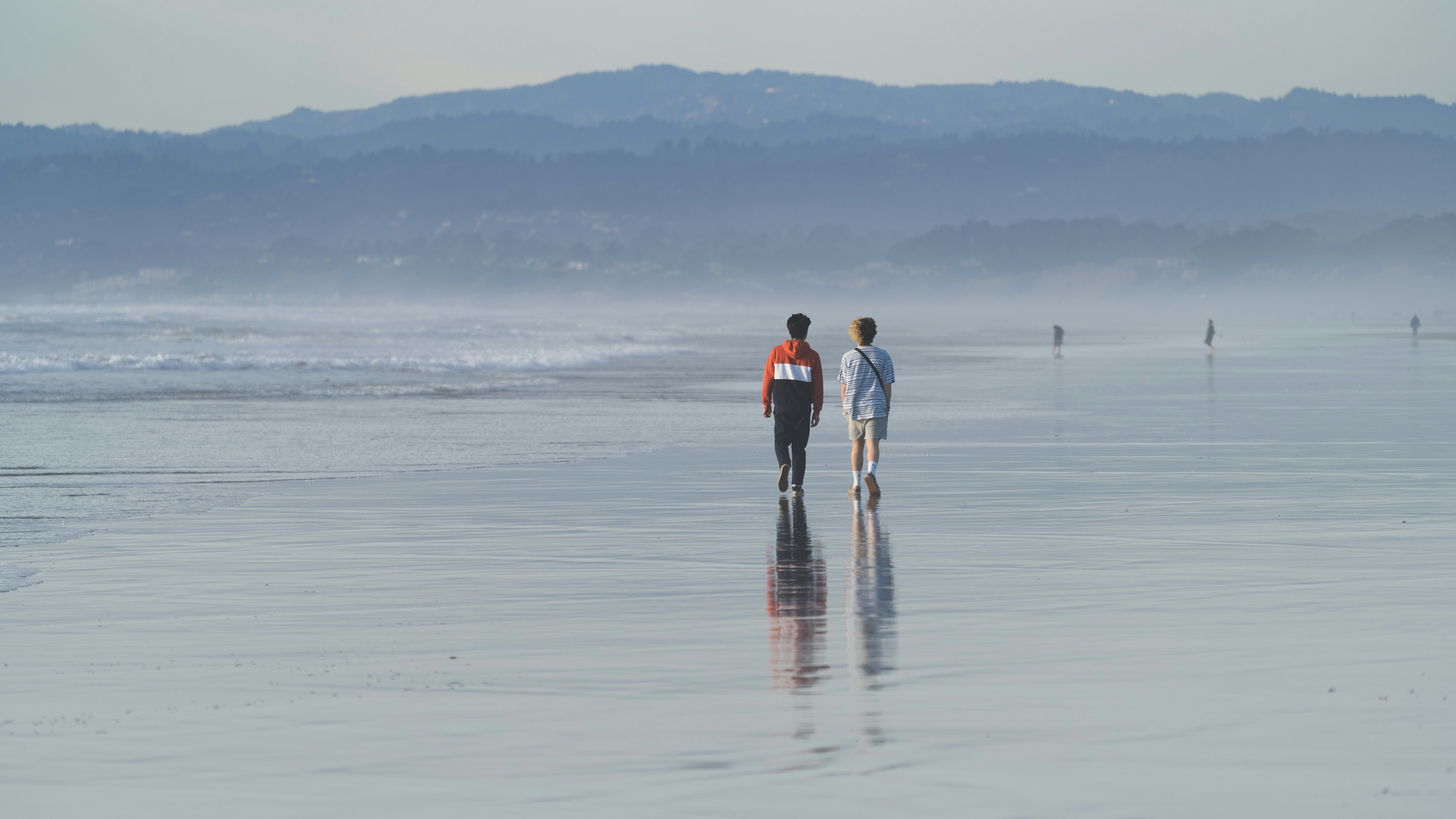 man and woman holding hands while walking on beach during daytime